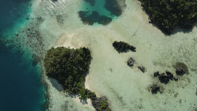 aerial shoot, flight over colourful lagoon with Turquoise water, sand beach and palm trees in Raja Ampat Indonesia
