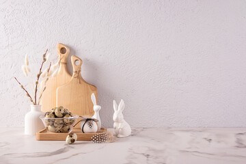 Kitchen stone countertop decorated for Easter in light colors. ceramic figurines of bunny, a vase with willow twigs, a bowl with quail eggs