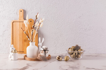 Kitchen festive background for Easter day. Eco-friendly kitchen utensils, a vase with willow sprigs, a bowl with quail eggs. Minimalist eco style.