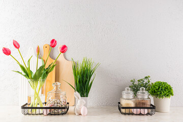 Stylish kitchen background decorated for Easter holiday. vase with tulips, potted plants, eggs on stands, ceramic rabbits. Front view.