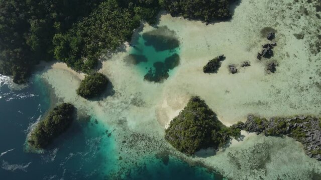 aerial shoot, flight over colourful lagoon with Turquoise water, sand beach and palm trees in Raja Ampat Indonesia