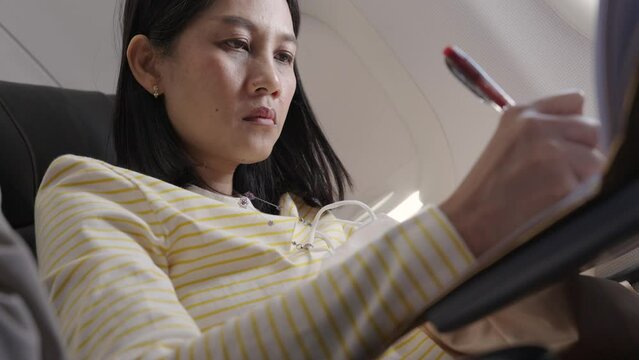 Female Asian tourist writes arrival card on seat to submit to immigration after getting off the plane.