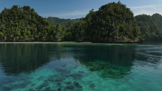 aerial shoot, flight over colourful lagoon with Turquoise water, sand beach and palm trees in Raja Ampat Indonesia