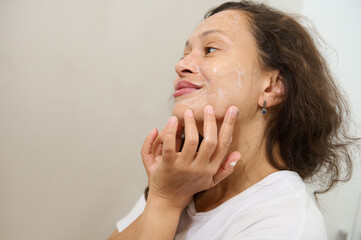 Close-up of a beautiful young woman applying cleansing gel on her face, removing makeup, smiling looking at the mirror