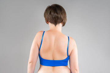 Female back, woman in blue bra on gray background, body care and correction of scoliosis concept