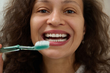 Happy woman smiling with beautiful toothy smile, holding a toothbrush near her face and looking at the camera