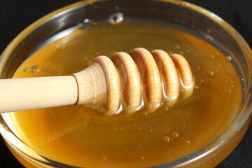 On a black background there is a glass plate with fresh honey and a special spoon.