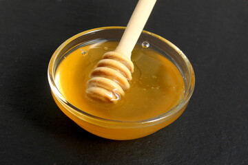 On a black background there is a glass plate with fresh honey and a special spoon.
