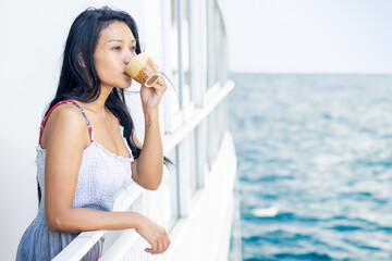 A woman in a summer dress drinks from a mug on board a cruise ship