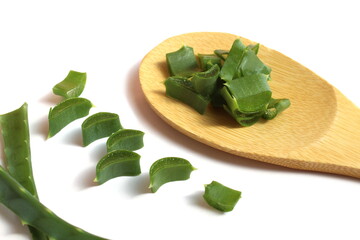 A wooden spoon with aloe leaves lies on a white background.