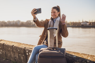 Happy woman  tourist with suitcase taking selfie  and waving while resting by the river. Toned...