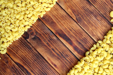 Dry pasta lies on a wooden background with space for text.