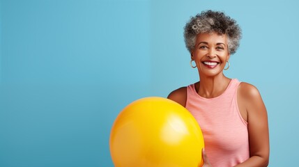 Ältere Frau mit gelbem Gymnastikball vor blauem Studiohintergrund