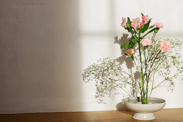 Beautiful pink and white flowers in bowl on rustic background. Tender floral composition on kenzan or flower pin in sunlight. Modern flower arrangement