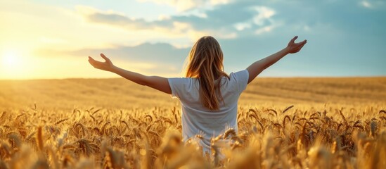 Young woman in wheat field, arms open to the sky, celebrating or meditating. - obrazy, fototapety, plakaty