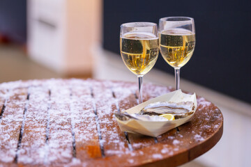 Two glasses of wine standing on a wooden, snowy table and a bowl of oysters in the foreground.