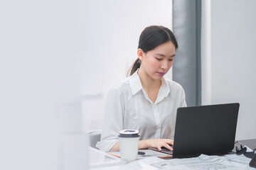 Portrait of a beautiful confident businesswoman using a laptop computer sitting in a modern office. Smiling Asian freelancer working online from home.