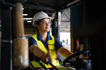 Fotobehang female factory worker. female forklift operator working in a warehouse. Portrait of young Indian woman driver sitting in forklift and smiling working in warehouse. © KANGWANS