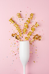 White champagne glass with confetti and party streamers on pink background. Minimal party concept.