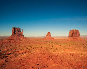 Monument valley landscape, Utah, USA, clear blue sky and long shadows. The three famous mittens, dirt road passing infront.