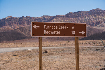 Road sign to Furnace Creek and Badwater in Death Valley, California, in bright sunlight, near the junction of road 190 and a dirt road towards Salt Creek trailhead.	