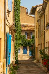 A street of the old town of Arles, in south France, mediterranean architecture, colored beige walls, green plants hanging on the walls. Hazy blue sky.