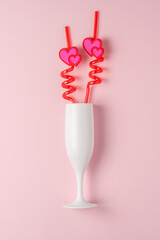White glass of champagne with hearts on a straw on a pink background. Love minimal concept.