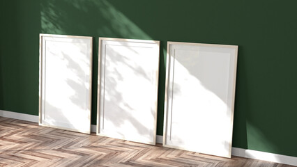 Three white blank mock-up photo frame canvases leaning against a green wall on a wood parquet floor in a room with sunlight casting soft tree shadows. 3D render