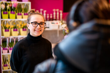 Portrait of smiling woman, flower shop owner, standing at her work place talking with customer