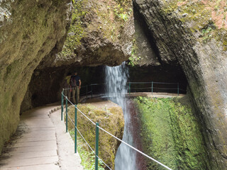 View of waterfall crossing the path at levada, water irrigation channel and tropical plants at hiking trail Levada do moinho to levada nova waterfall. Madeira, Portugal