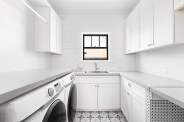 A renovated white laundry room with a mosaic tile floor, grey marble countertops, white appliances,...