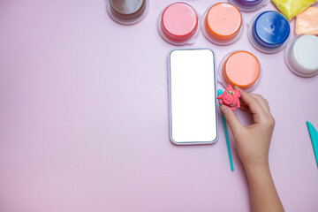 Smartphone with blank screen, air dry clay and a plasticine figure in a child's hand on a pink...