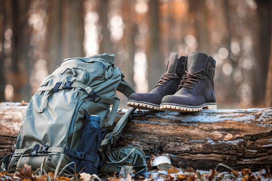 Hiking equipment in forest. Backpack with thermos and leather ankle hiking boots