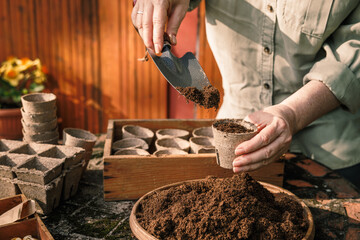 Gardener with shovel putting soil and compost into biodegradable peat pots. Planting and sowing...
