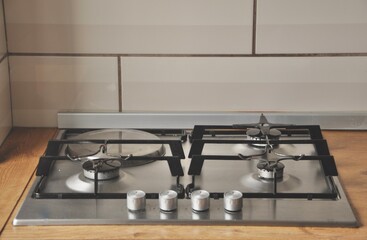 Stainless steel gas cooker built in wooden countertop at contemporary kitchen. Gas hob in beige scandinavian kitchen.