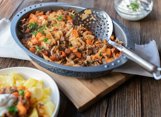 Minced meat pan with cabbage and vegetables in a roasting pan on wooden table