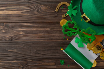 Irish festivities captured: Overhead shot of leprechaun hat, letter, party glasses, lucky horseshoe, gold coins, trefoils, confetti on wooden background with empty space for text