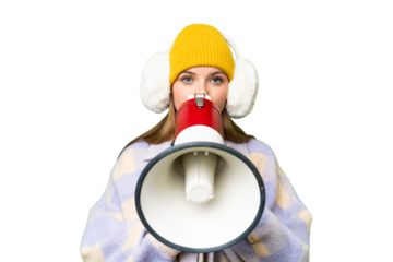 Young blonde woman wearing winter muffs over isolated chroma key background shouting through a megaphone
