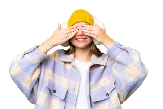 Young blonde woman wearing winter muffs over isolated chroma key background covering eyes by hands