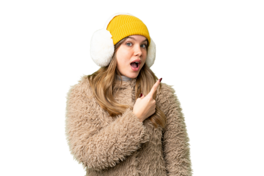 Young girl wearing winter muffs over isolated chroma key background surprised and pointing side
