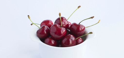 Red cherry in the white bowl on the white background. Close-up. Copy space.