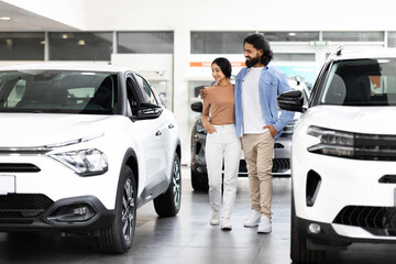 Happy millennial spouses choosing modern auto at showroom