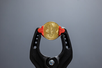 Construction vice holding golden Bitcoin isolated on grey background. Golden bitcoin cryptocurrency...