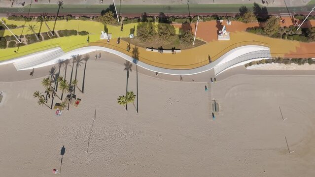 Drone aerial view of Benidorm west beach promenade showing people walking and long shadows of palm trees