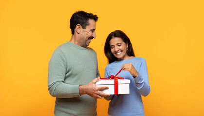 A delighted woman in a blue sweater gracefully accepts a white gift box with a red ribbon
