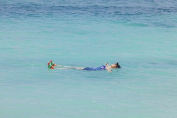 View of woman in swimsuit lying on back on blue surface of Caribbean Sea on island of Aruba.