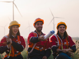 Group of maintenance engineers preparing and planning inspection of wind turbines, holding tablets, looking at wind turbines