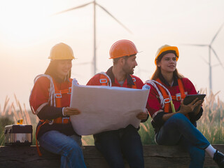 Group of maintenance engineers preparing and planning inspection of wind turbines, holding tablets,...