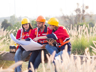 Group of maintenance engineers preparing and planning inspection of wind turbines, holding tablets, looking at wind turbines