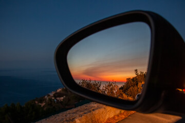 Closeup of a sunset in nature seen from the side mirror of stopped car